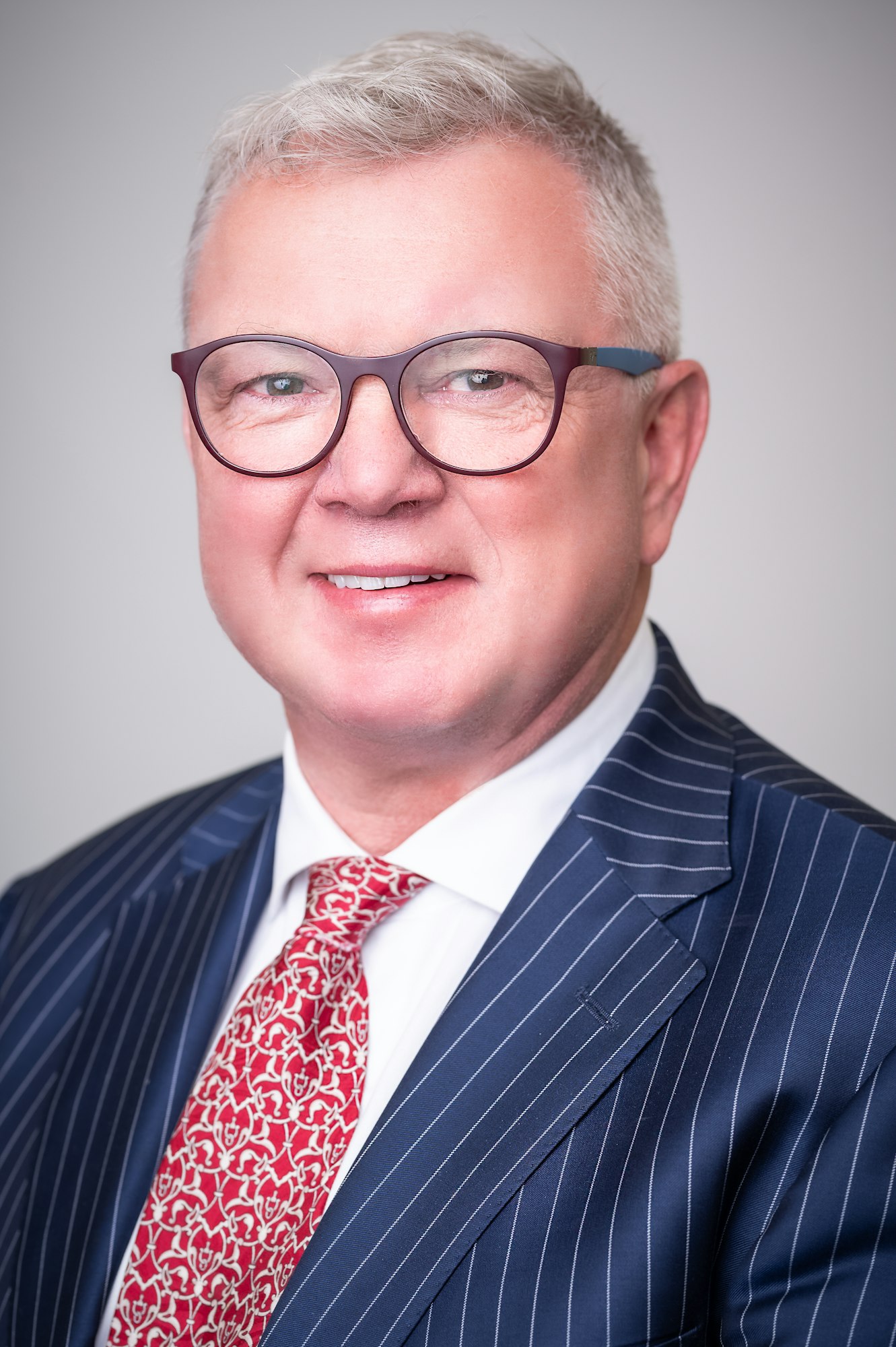 Photo of Kevin B. Lindahl wearing a blue pinstriped suit jacket and red and pink tie.